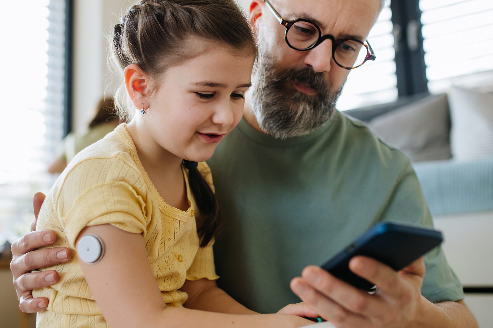dad and daughter checking phone while daughter wears a diabetes glucose monitor
