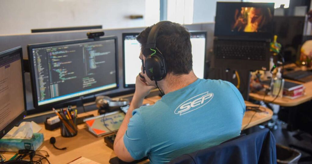 Software developer in SEP t-shirt examines code on computer screen
