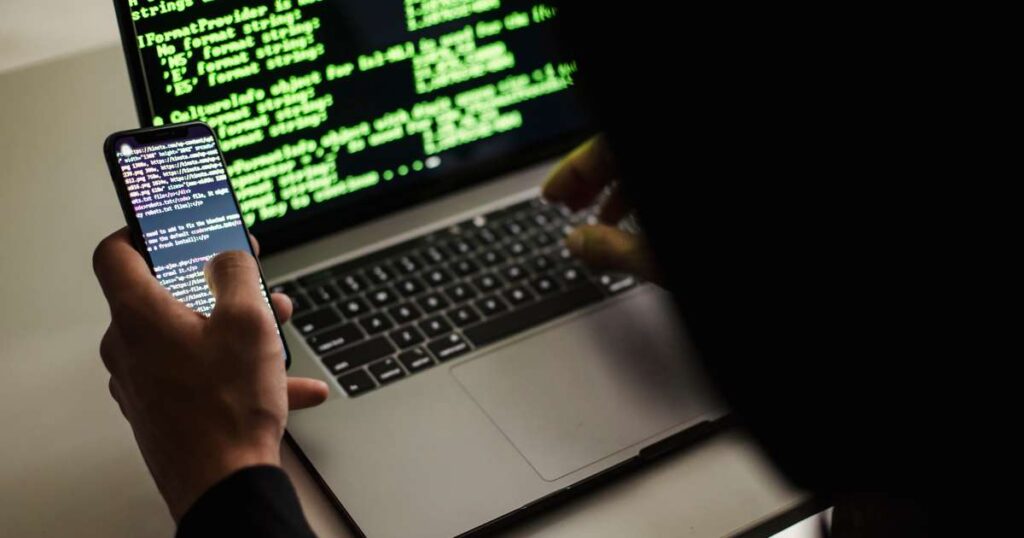 Developer looking at code on laptop and mobile phone screens