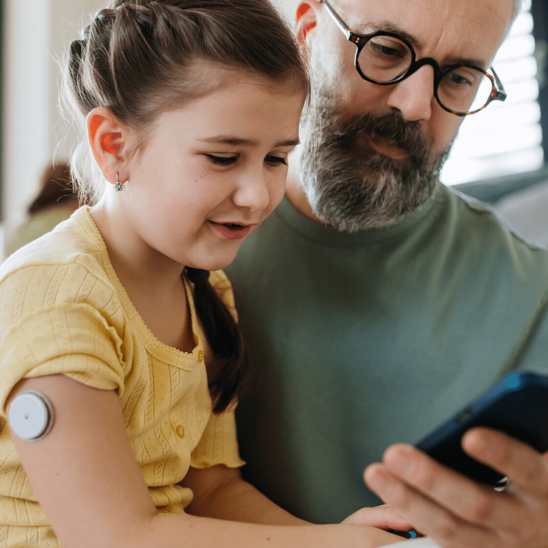 dad and daughter checking phone while daughter wears a diabetes glucose monitor